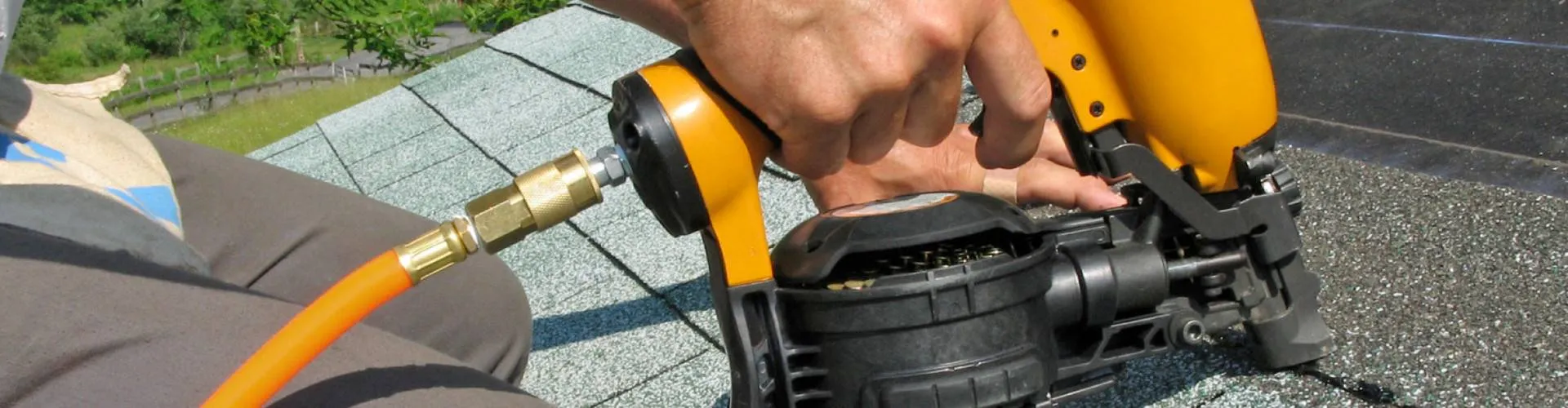 Roofer fastening asphalt shingles with a pneumatic nail gun