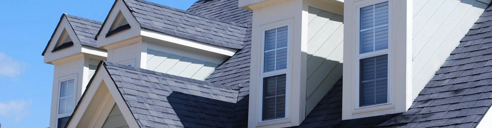 Grey shingle roof with dormer windows under a blue sky